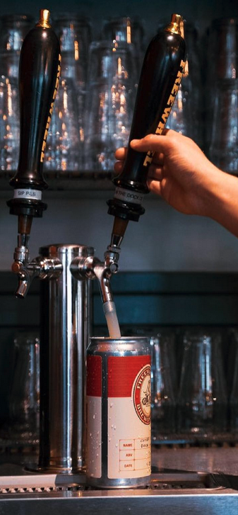 A beer tap pouring beer into a can with the Freewheel logo on it.