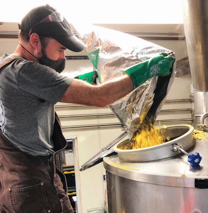 A brewer is pouring mashed malted barley into a fermentation tank.