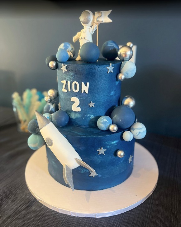 A birthday cake for a child named Zion. It's space-themed, with planets, a spaceship, and an astronaut on top.