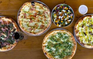 Pizzas with different toppings and a salad on a table.