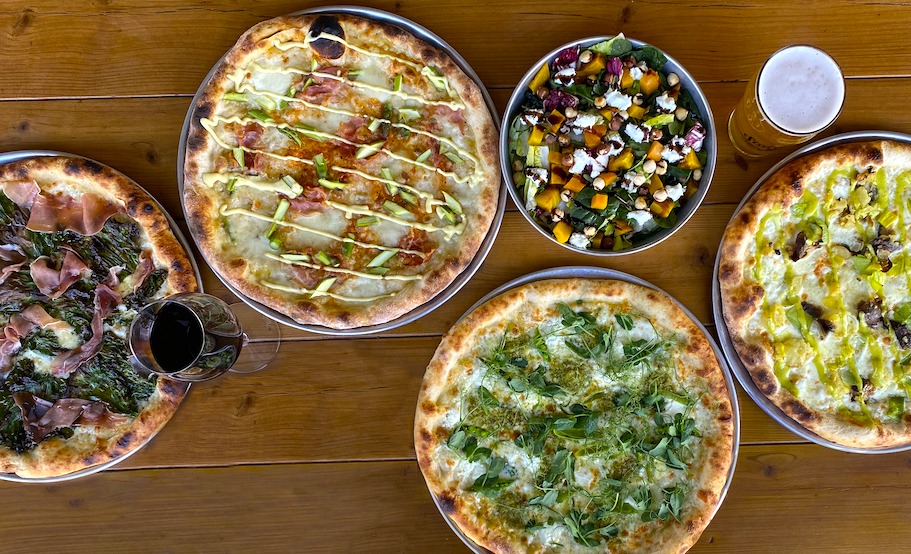 Pizzas with different toppings and a salad on a table.