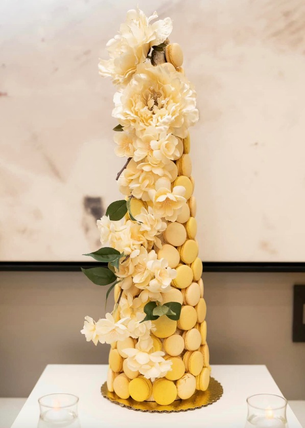 A cone-shaped cake made up of macarons, embellished with white flowers.