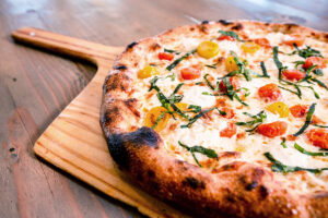 A pizza topped with tomatoes and herbs atop a wooden paddle.