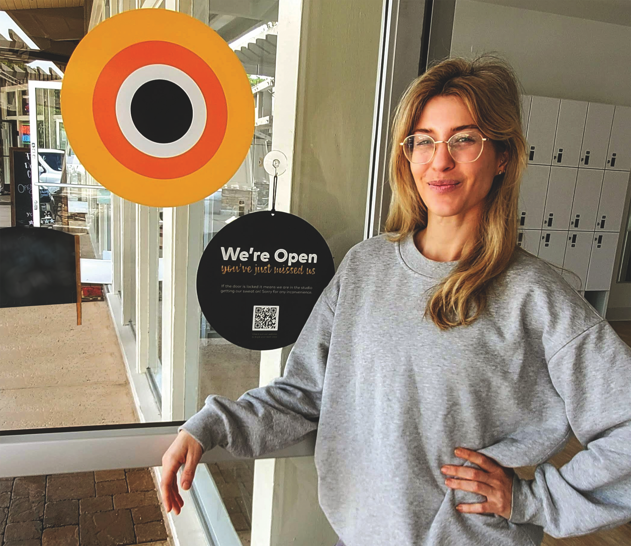 A CorePower employee next to some lockers and a sign that says "We're open."