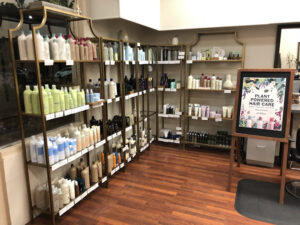 Various Aveda hair products organized on shelves. A sign beside them reads "Plant powered hair care."