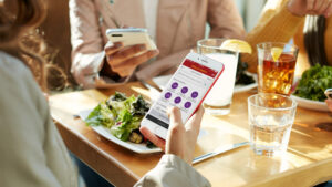 Close up of an individual viewing the Wells Fargo mobile app on a phone while dining at a table with two other persons.